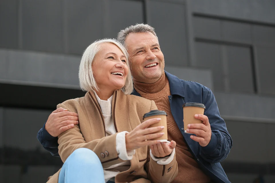 Pareja de jubilados sonriendo con un café al aire libre